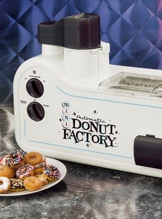 a donut factory machine sitting on top of a counter next to plates of doughnuts