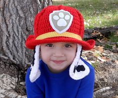 a young boy wearing a fireman hat and blue shirt sitting in front of a tree