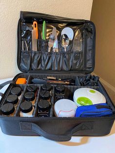 an open black suitcase filled with kitchen utensils and other items on top of a table