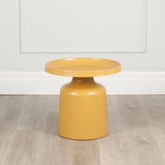 a yellow stool sitting on top of a hard wood floor next to a white wall