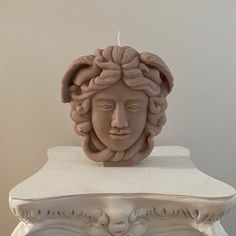 a statue of a woman's head on top of a white pedestal with a candle in it