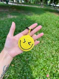 a hand holding a yellow smiley face keychain in the middle of a grassy area