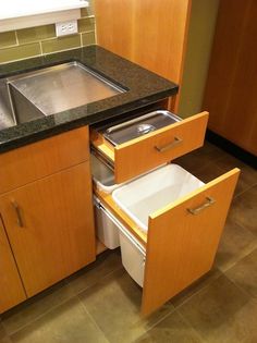 a kitchen with a sink, dishwasher and trash can in the middle of it