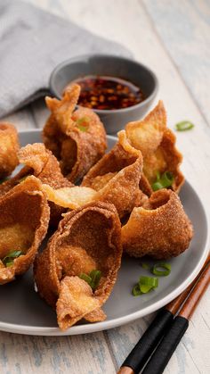 some fried food is on a plate with chopsticks and sauce in the background