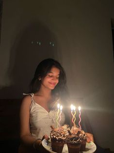 a woman holding a plate with two cupcakes and lit candles on it in front of her