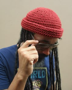 a man with dreadlocks is wearing a red hat and holding his glasses to his face