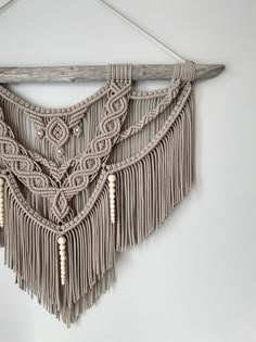 a macrame wall hanging with beads and tassels on a white wall