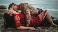 a man and woman laying on the beach with their arms around each other while they are kissing