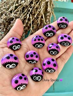 purple and black decorated rocks with eyes on them are held in someone's hand