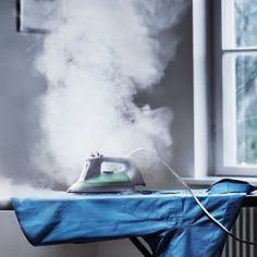 an ironing board with steam coming out of it, in front of a window