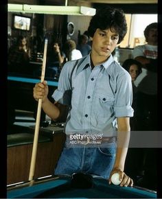 a young man holding a pool cue in his hand while standing next to a pool table