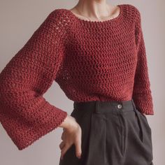 a woman wearing a red crochet sweater and black pants with her hands on her hips