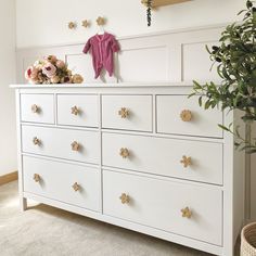 a white dresser with flowers and a pink shirt on top