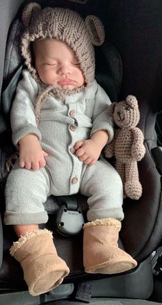 a baby sleeping in a car seat with a teddy bear