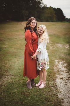 two women standing next to each other in a field with grass and trees behind them