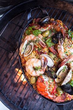 a pan filled with seafood and rice on top of a grill