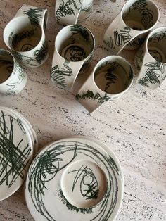 several cups and saucers are sitting on a table with green ink drawn on them