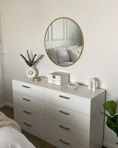 a bedroom with white furniture and a round mirror on the wall above it's dresser