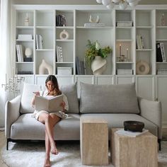 a woman sitting on a couch reading a book in front of some bookshelves