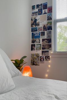 a bed with white sheets and pillows next to a window covered in pictures on the wall