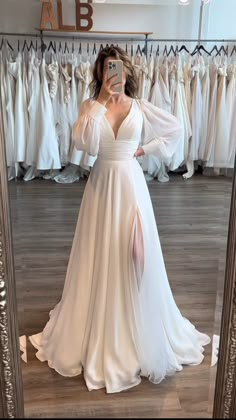 a woman taking a selfie in front of a mirror wearing a white dress with long sleeves