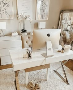 a white desk topped with a computer monitor next to a mirror and vase filled with flowers