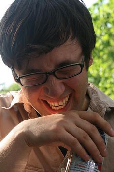 a man with glasses is smiling and eating something out of a plastic container in front of him