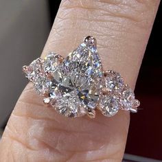 a woman's hand holding an engagement ring with three pear shaped diamonds