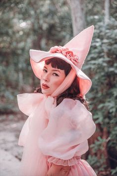 a woman wearing a pink hat and dress in the woods with her hands on her hips