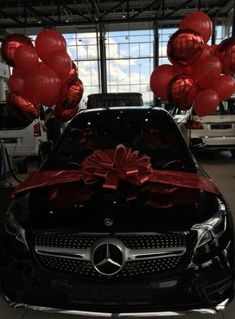 red balloons are tied to the hood of a black car in a showroom with other cars