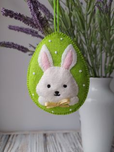 a green felt ornament with a white rabbit on it and purple flowers in the background