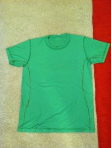 a green t - shirt laying on top of a red and white towel next to a pair of scissors