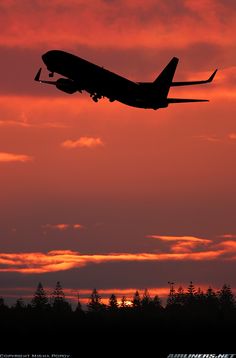 an airplane is flying in the air at sunset or dawn with clouds and trees behind it