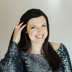 a woman smiling and wearing a sequined top with her hands on her head