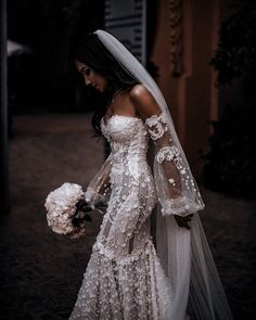 a woman in a wedding dress is holding a bouquet and walking down the street with her veil over her head