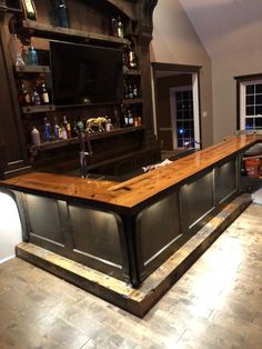 a bar in the middle of a room with shelves on either side and an overhead television above it