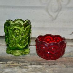 two green and red glass bowls sitting on top of a wooden table next to each other