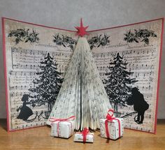 an origami christmas tree with presents under it on a wooden table next to a sheet of music