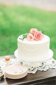 a white wedding cake with pink roses on top and lace doily around the edges