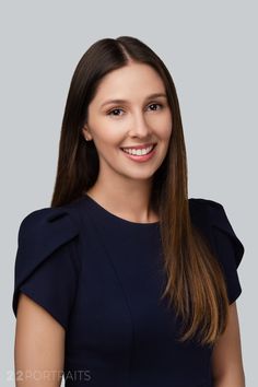 a woman with long brown hair wearing a blue dress and smiling at the camera while standing in front of a gray background