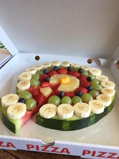 a fruit pizza with sliced bananas, kiwis and strawberries on it in a box