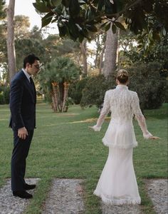 a man and woman in formal wear standing next to each other on the grass with palm trees behind them