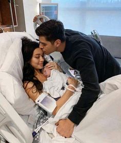 a man kissing a woman on the cheek in a hospital bed while holding a baby