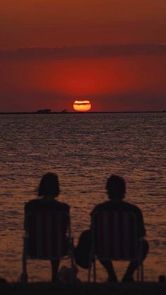 two people sitting on lawn chairs watching the sun set