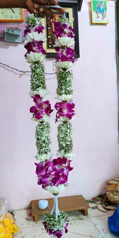 purple and white flowers are hanging from a pole in front of a wall with pictures on it