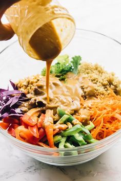 someone pouring dressing over a colorful salad in a bowl