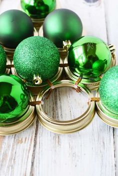 green christmas ornaments sitting on top of each other in gold rings and metal holders with ribbons