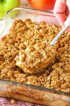 a person is spooning some food out of a casserole dish with apples in the background