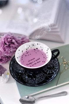 a black and white coffee cup sitting on top of a table next to purple flowers