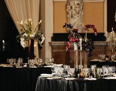 the table is set with wine glasses, silverware and flowers in tall vases